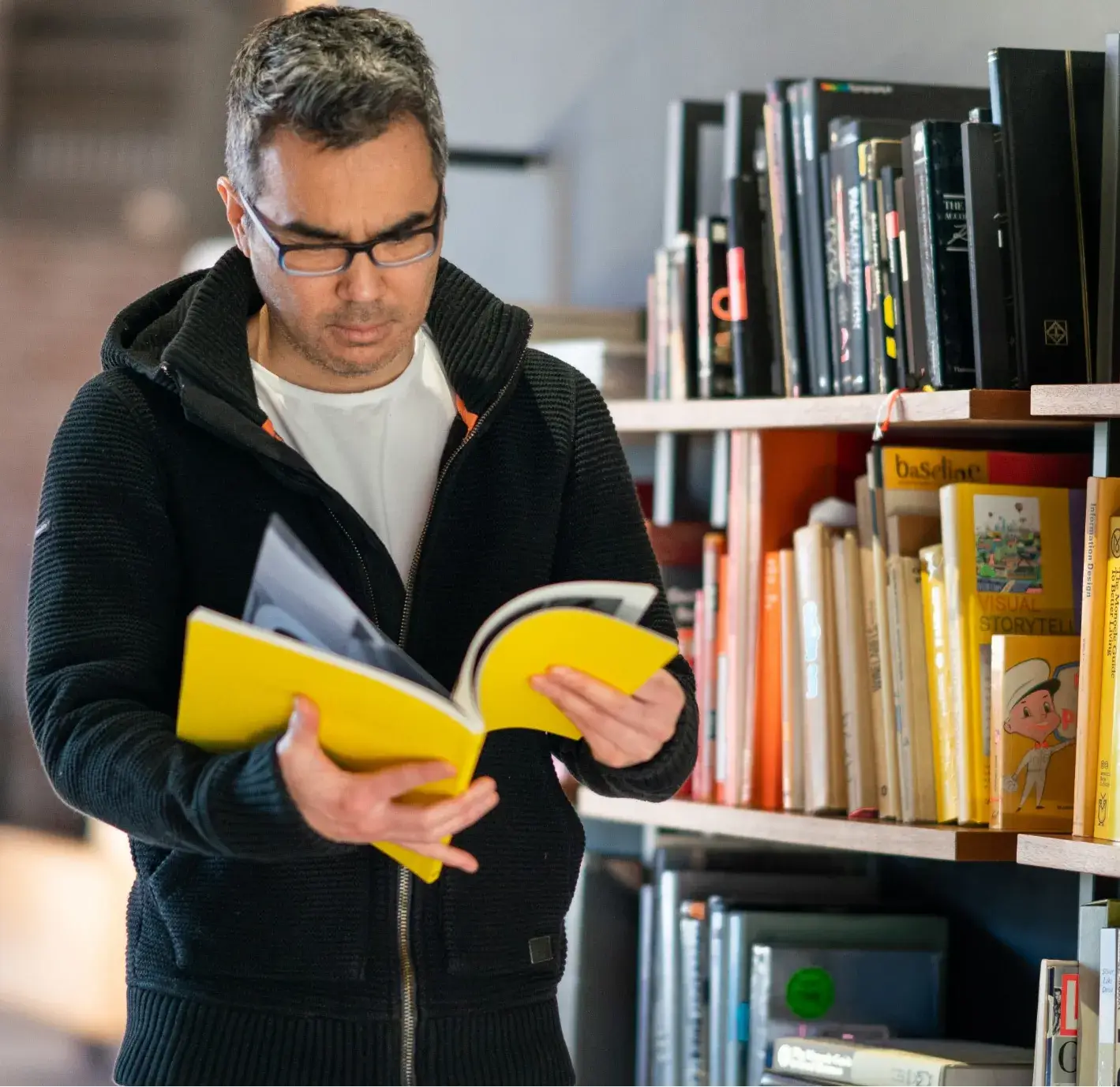 Luis Furushio reading a book related to architecture, surrounded by a bookshelf filled with design resources.